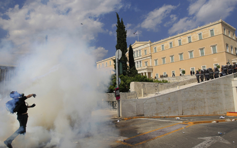 A protester throws back a tear gas canister at policemen in front of the parliament during violent protests in Athens' Syntagma square